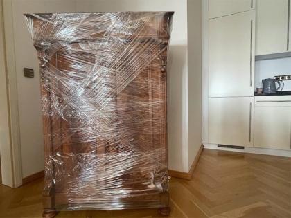 Ein antiker Holzschrank, sorgfältig mit transparenter Schutzfolie verpackt, in einem Raum mit Parkettboden und Kücheneinrichtung