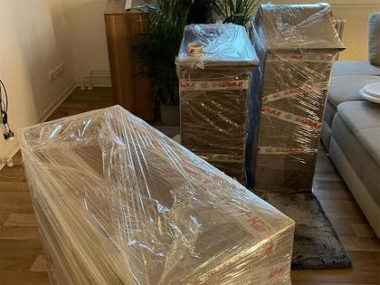 Mehrere Kommoden, sorgfältig mit transparenter Schutzfolie und Umzugsklebeband verpackt, in einem Wohnzimmer