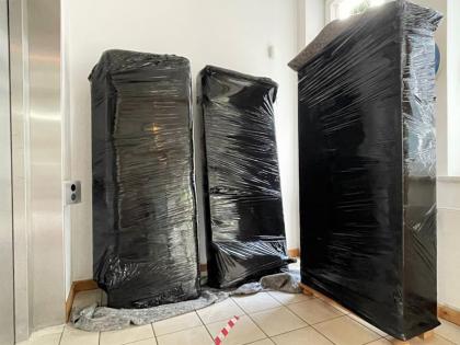 Drei Schränke, sorgfältig mit Schutzfolie verpackt, bereit für den Transport, neben einem Aufzug